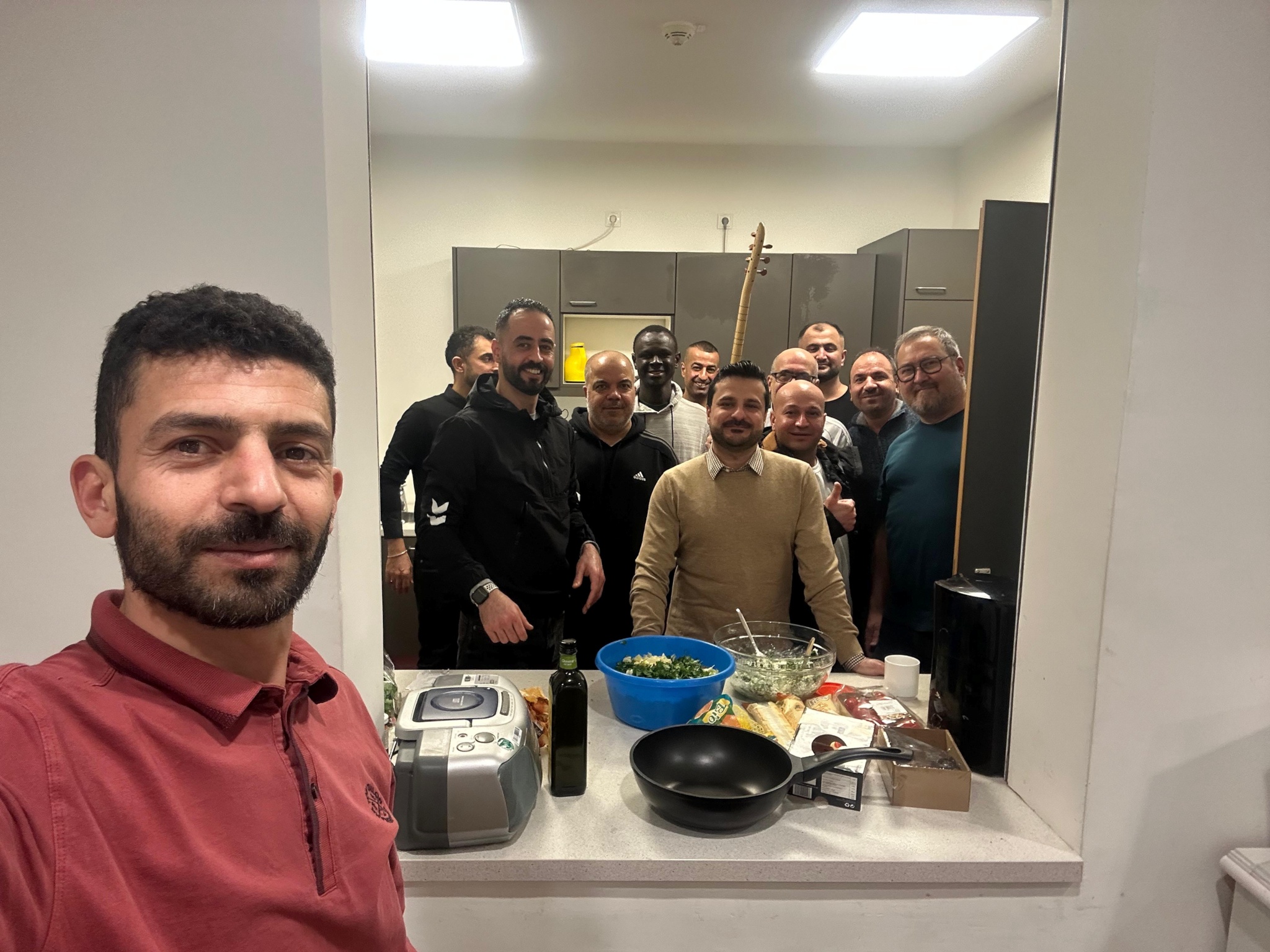 Ein Mann steht vor einem Spiegel, in der Spiegelung ist eine lachende Gruppe zu sehen